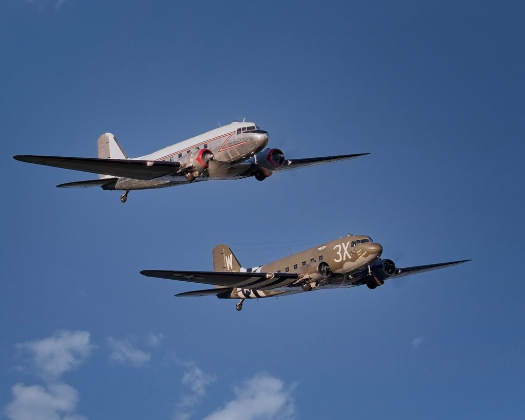 A civilian Douglas DC-3 and the C-47 That’s All, Brother flying together against a blue sky.